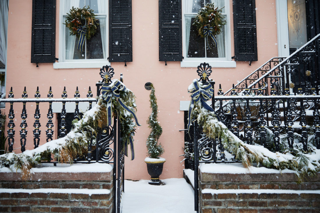 A pink home with snow-laden wreaths and snow on the ground