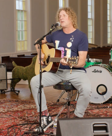 A man playing a guitar and singing while seated