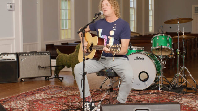 A man playing a guitar and singing while seated