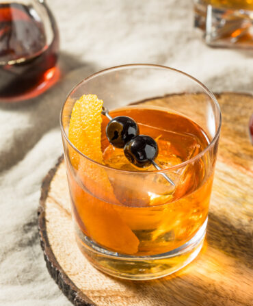 A bourbon cocktail with an orange peel and cherries