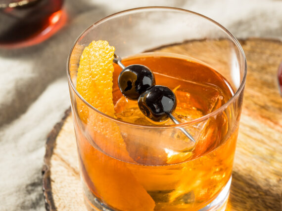 A bourbon cocktail with an orange peel and cherries