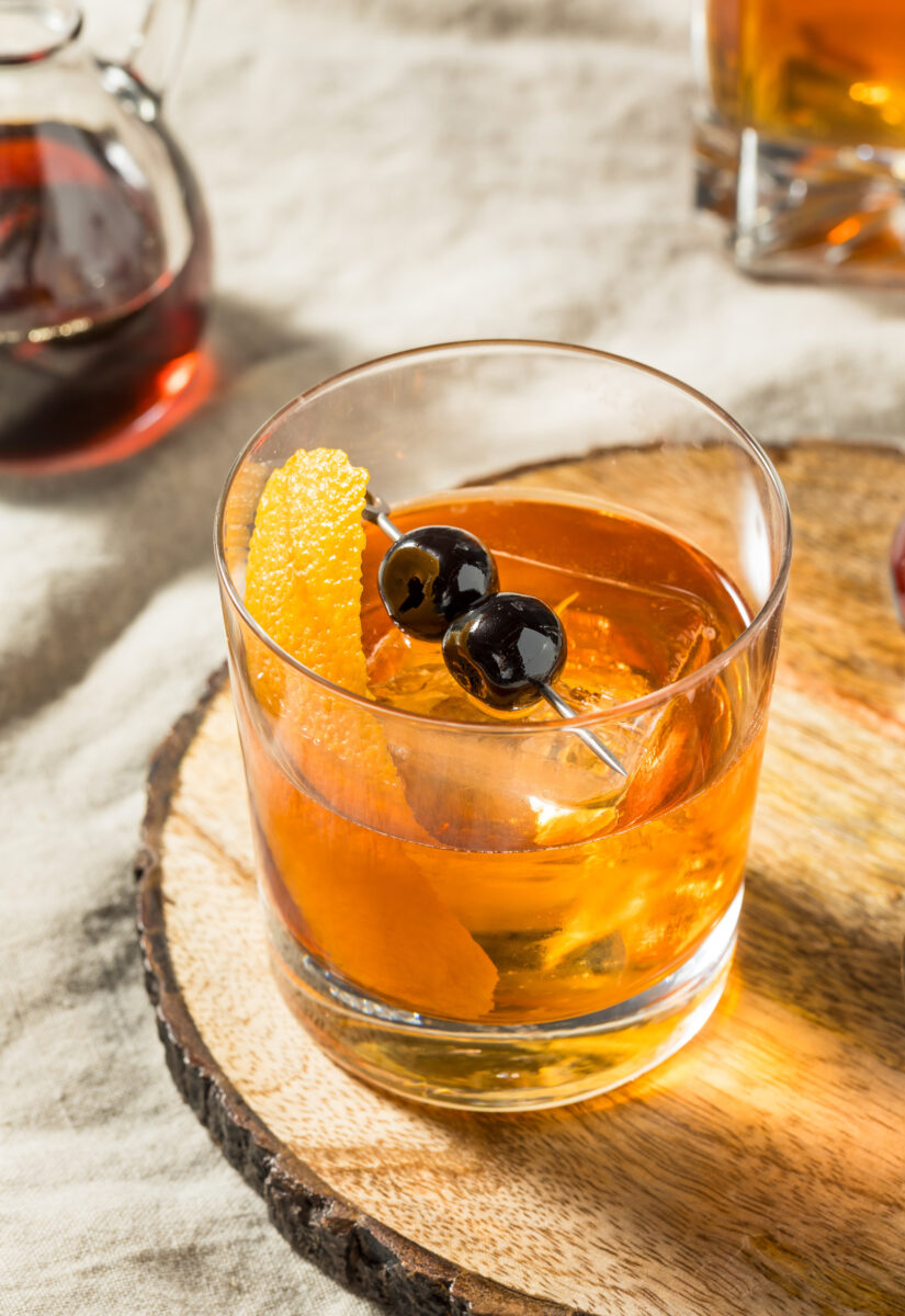 A bourbon cocktail with an orange peel and cherries