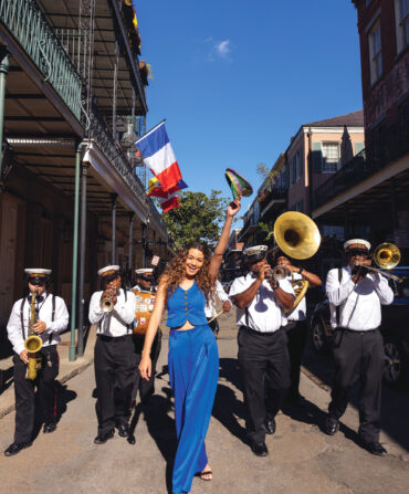 A woman in a blue suit strolls down a New Orleans street with a brass band