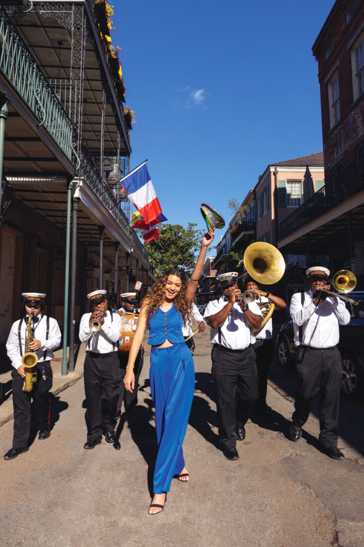 A woman in a blue suit strolls down a New Orleans street with a brass band