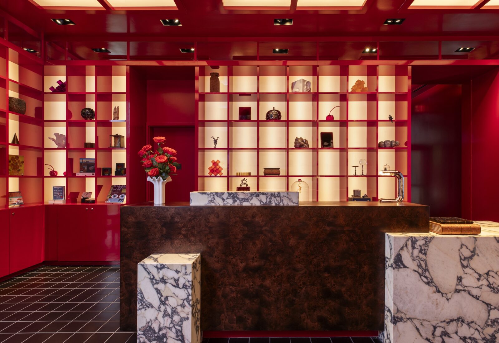 Inside a red hotel lobby with marble tables and shelves of art