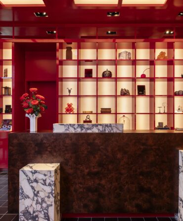 Inside a red hotel lobby with marble tables and shelves of art