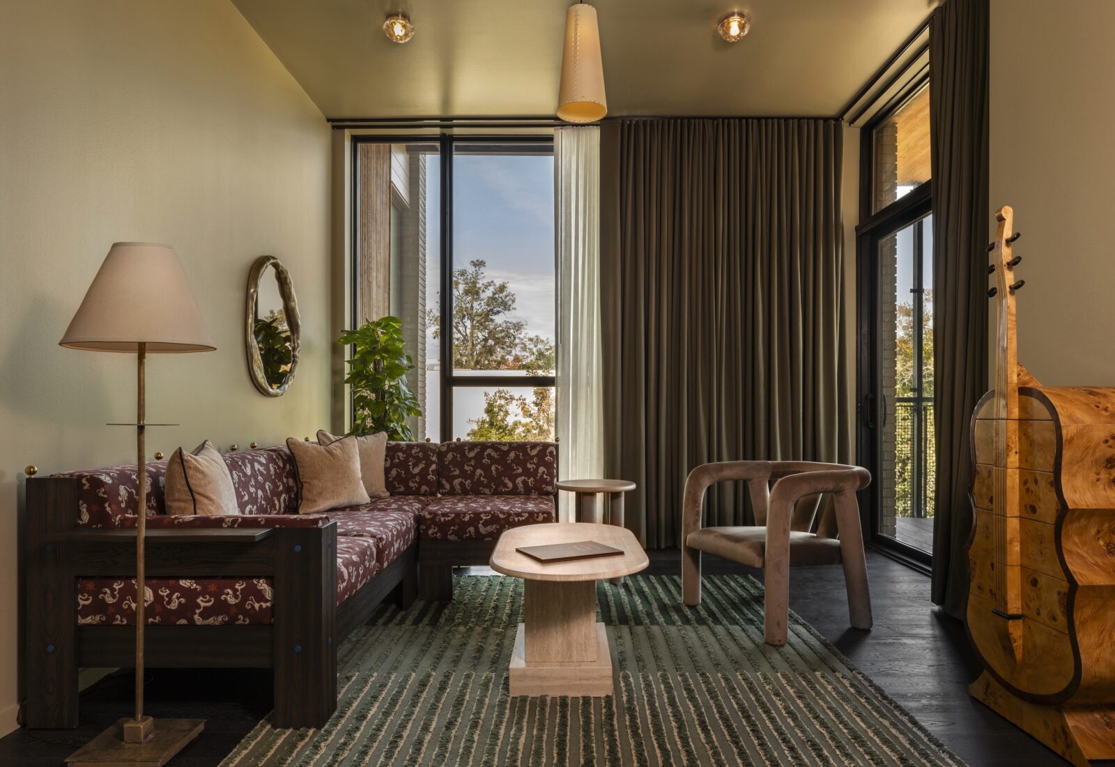 A seating area in a room with sculptural furniture and plum-colored, printed couch