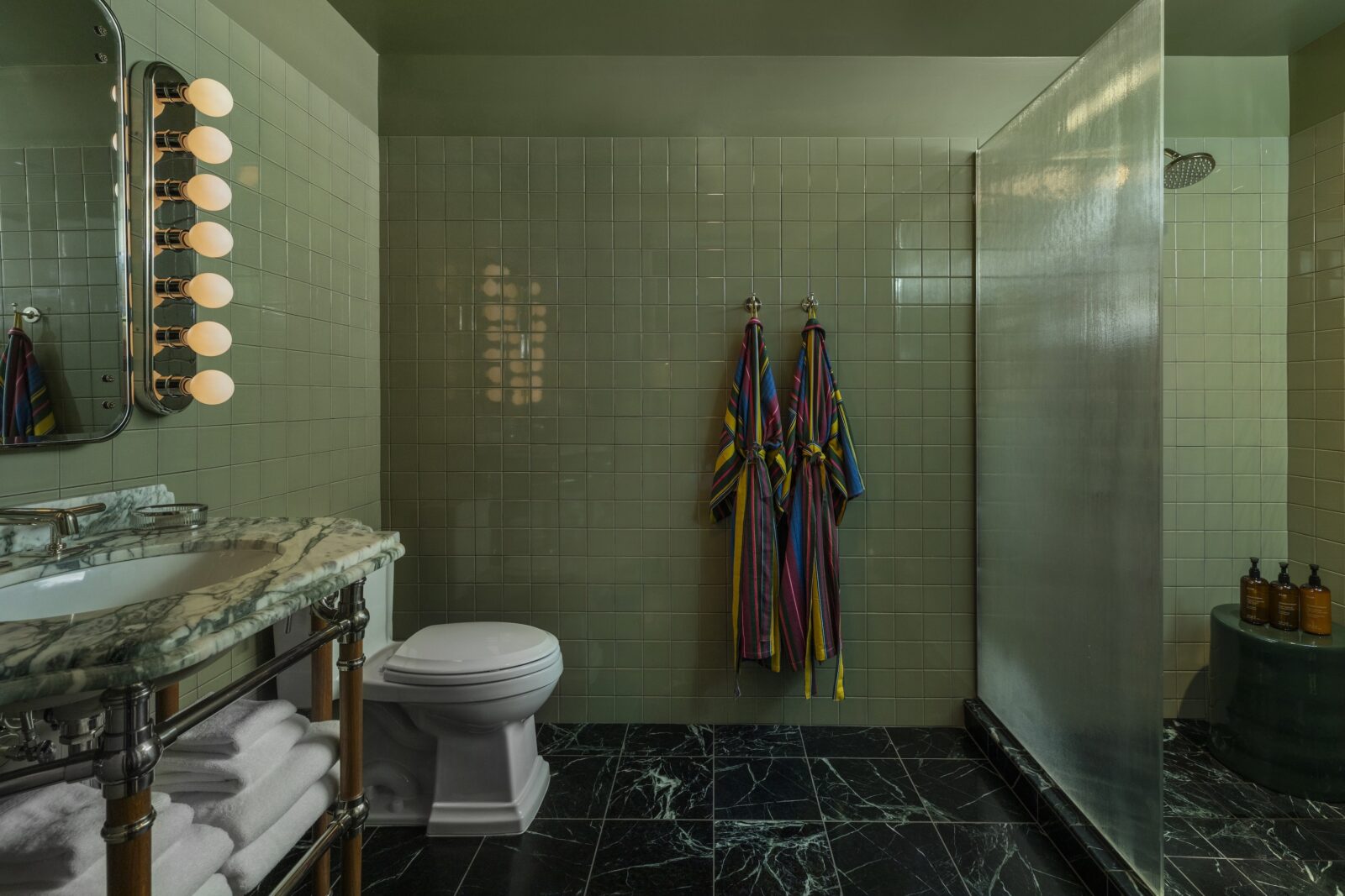 A safe green tiled bathroom with stone countertops and marble floors in a dark green-black