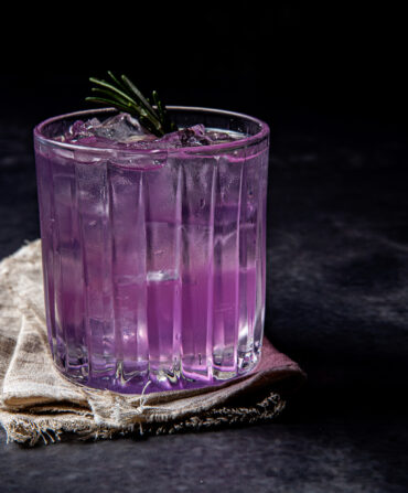 A purple cocktail with a sprig of rosemary