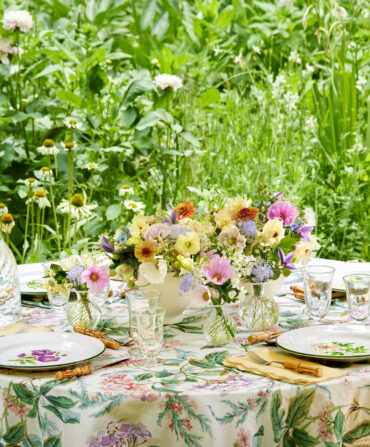 An outdoor table set with a floral table cloth and flowers