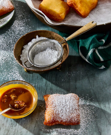 A table with beignets, powdered sugar, and a bowl of caramel sauce