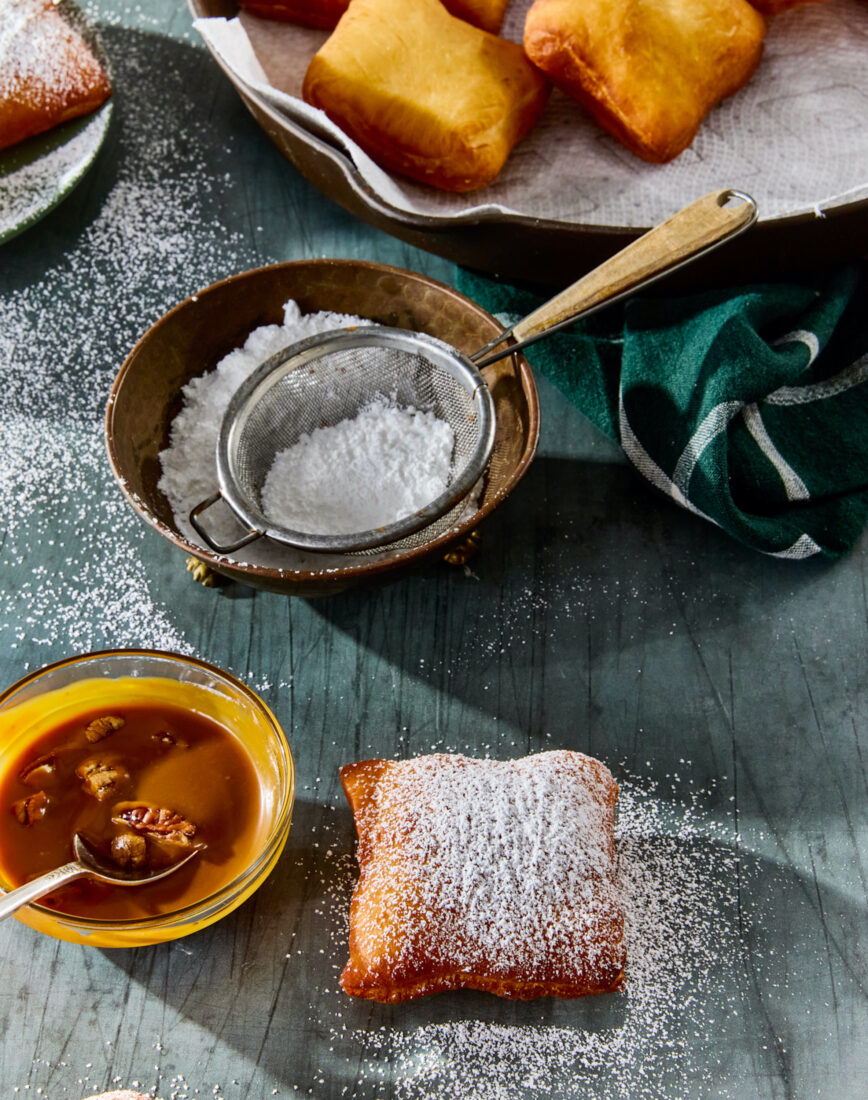 A table with beignets, powdered sugar, and a bowl of caramel sauce