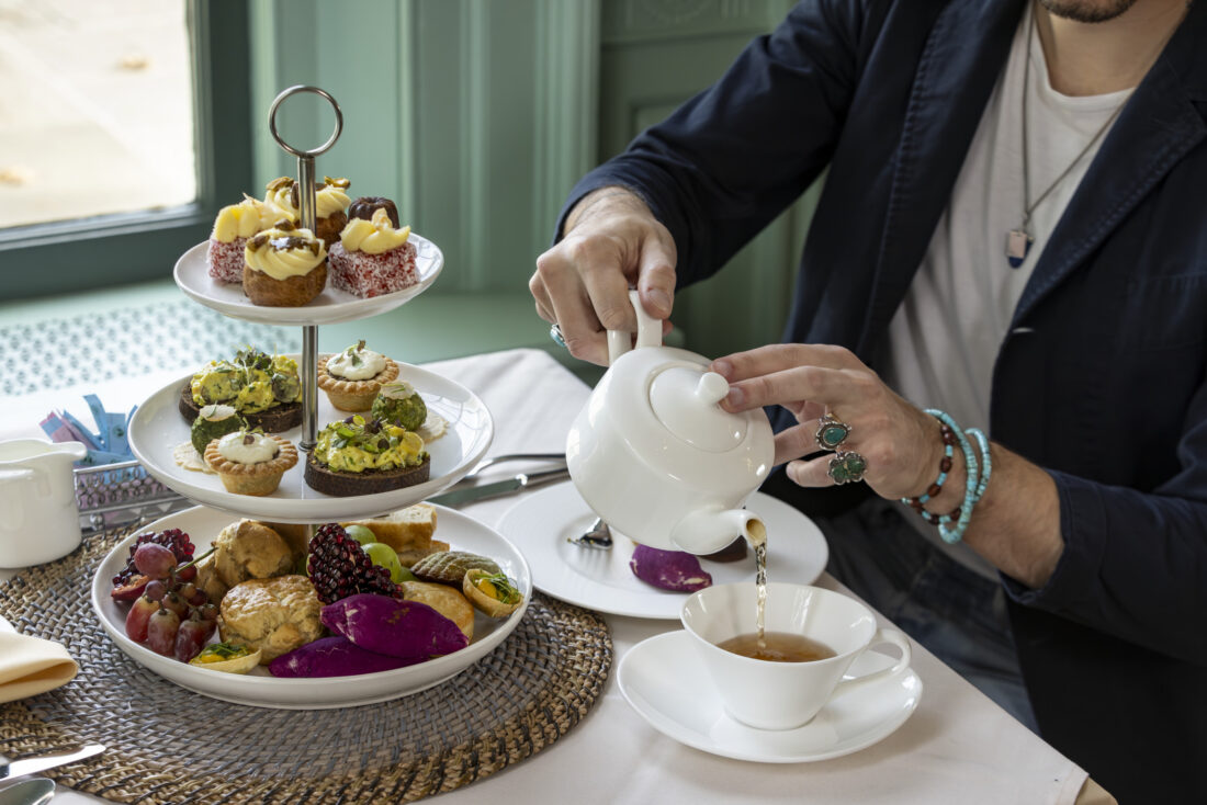 A person pours tea at a table with snacks