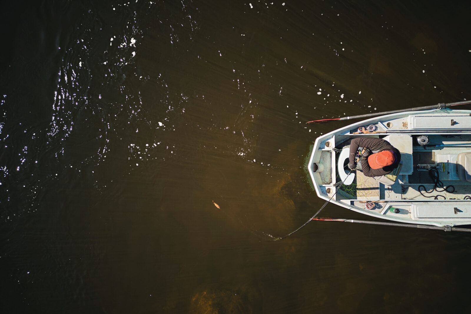 An aerial image of a boat on the water with a man fishing