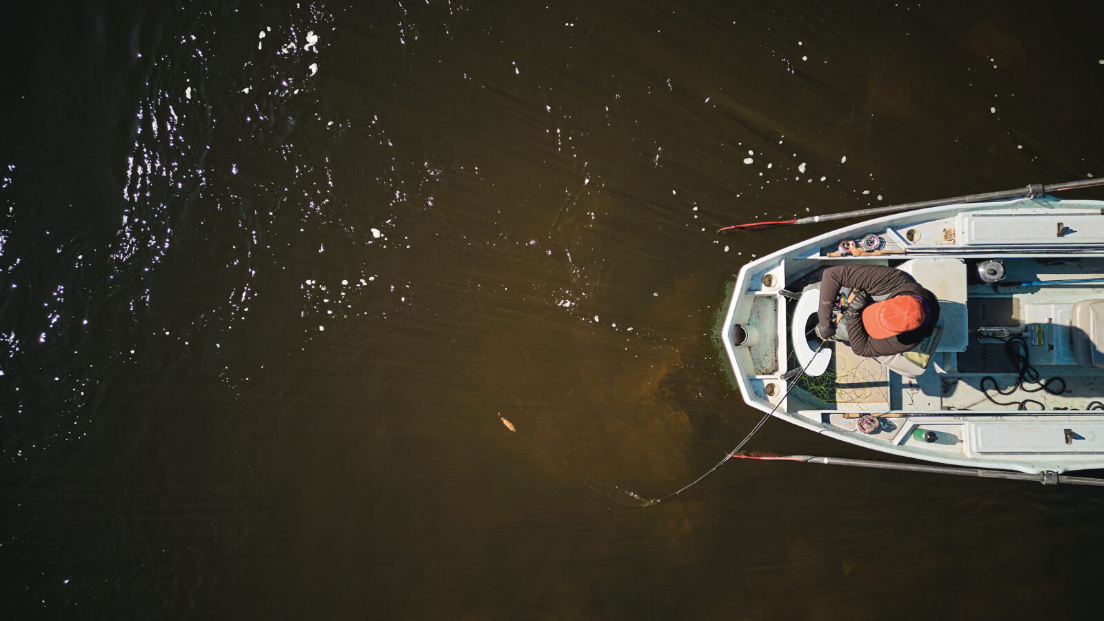 An aerial image of a boat on the water with a man fishing