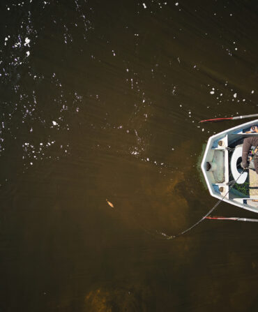 An aerial image of a boat on the water with a man fishing