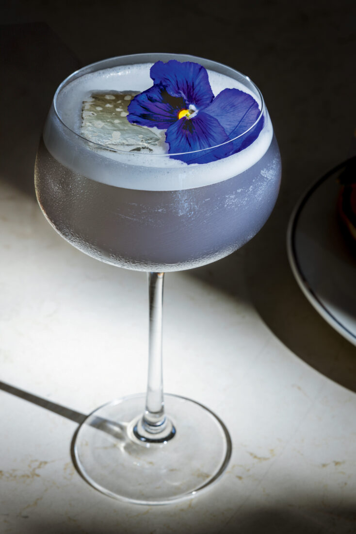 A blue cocktail with a blue violet flower on top