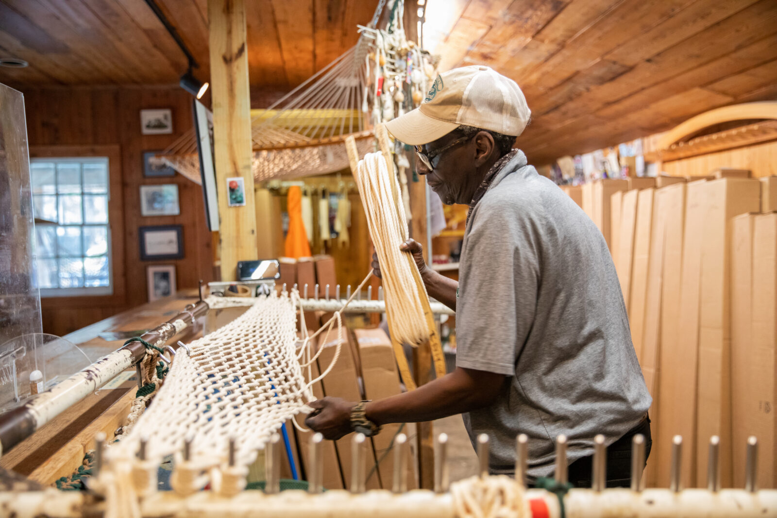 A man weaves a hammock on a stand in a shop