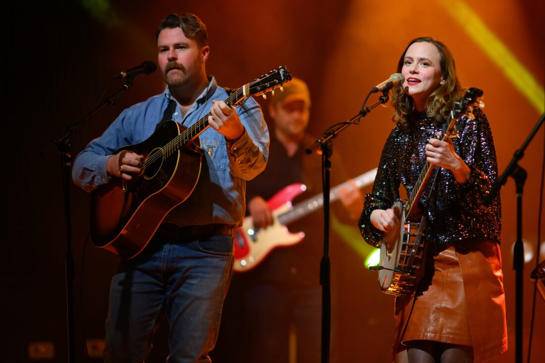 A man and a woman with guitars sing on stage