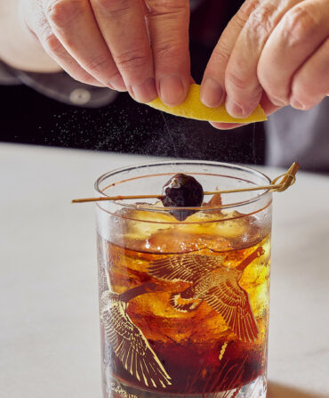 A hand twists a lemon peel over an old-fashioned