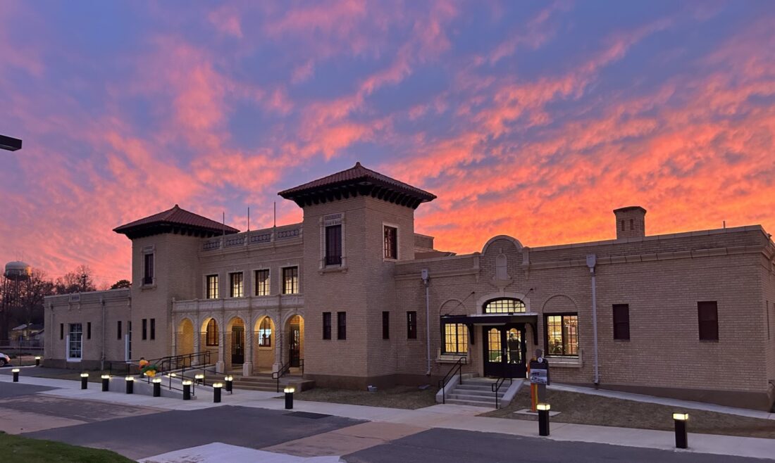 An old yellow brick Italianate and Spanish Revival building against a sunset