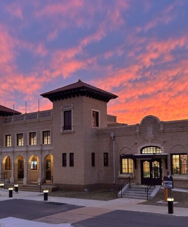 An old yellow brick Italianate and Spanish Revival building against a sunset