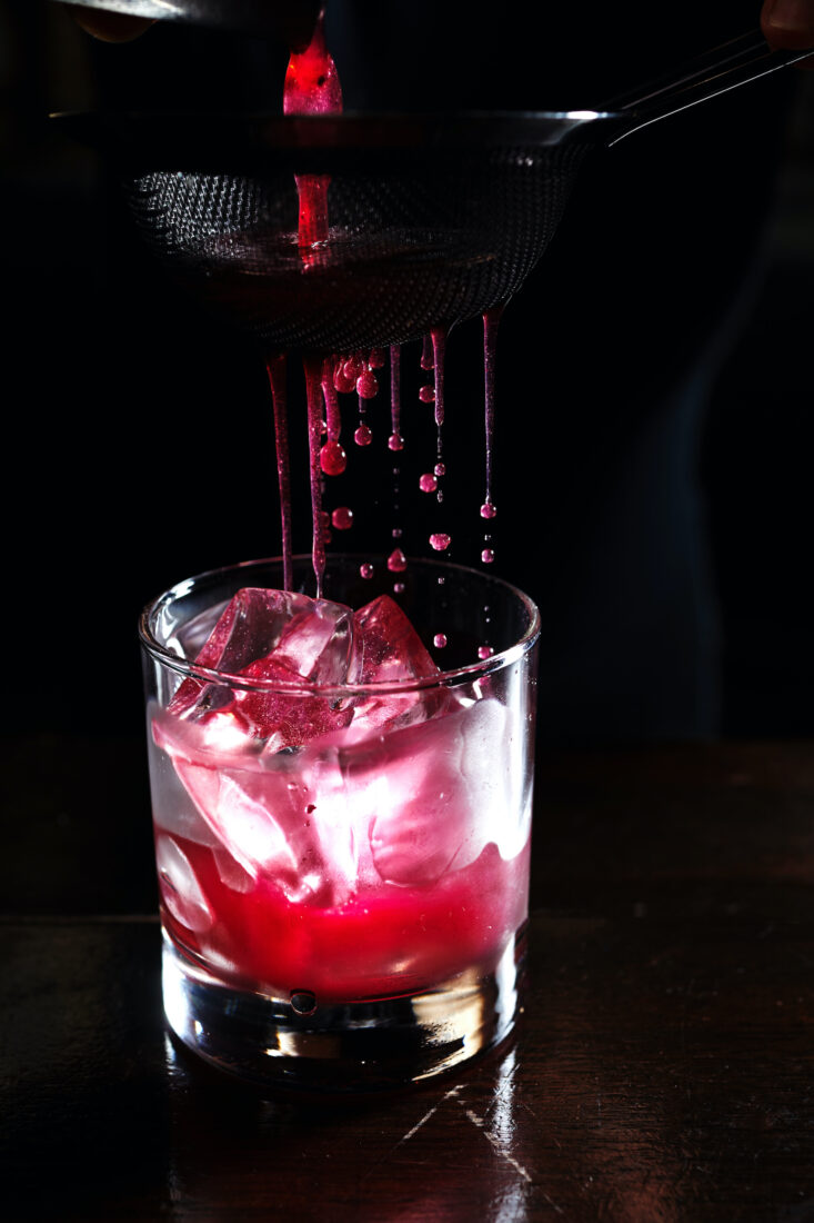 Red juice strains into a cocktail glass
