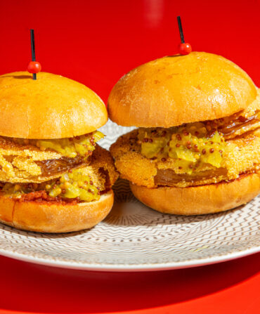 Two fried green tomato sliders on a white plate against a red background