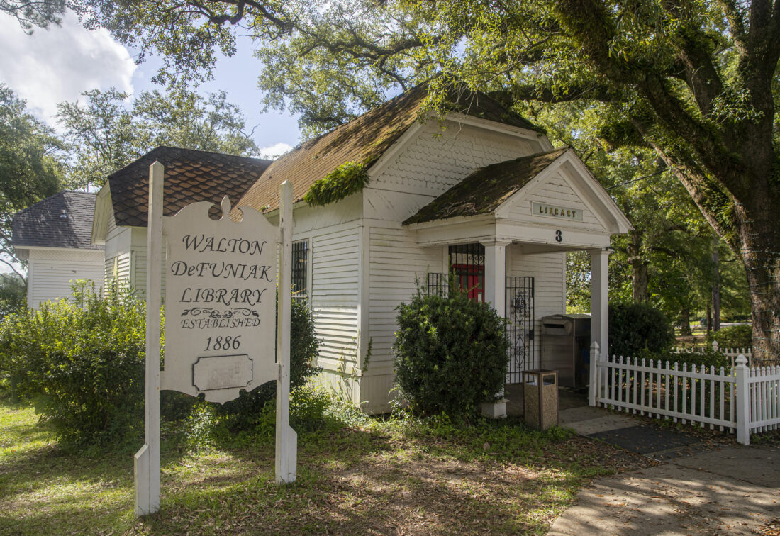 Outside a small white house which acts as a library. It sits under a canopy of trees