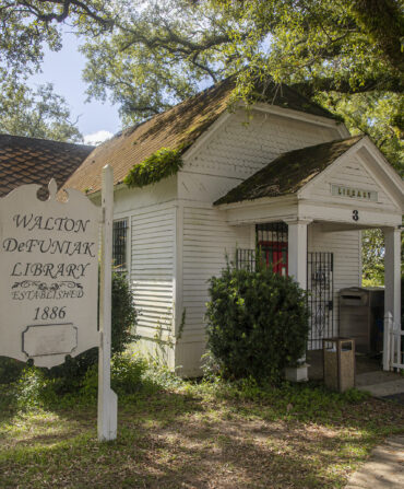 Outside a small white house which acts as a library. It sits under a canopy of trees