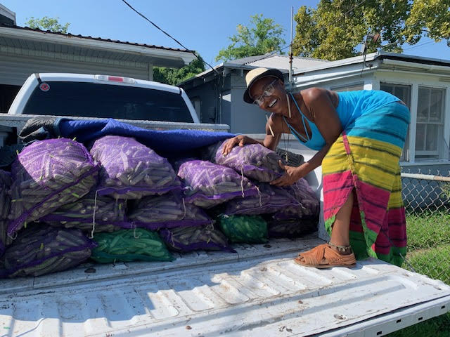 A woman stands on the bed of a truck with bags of harvested okra