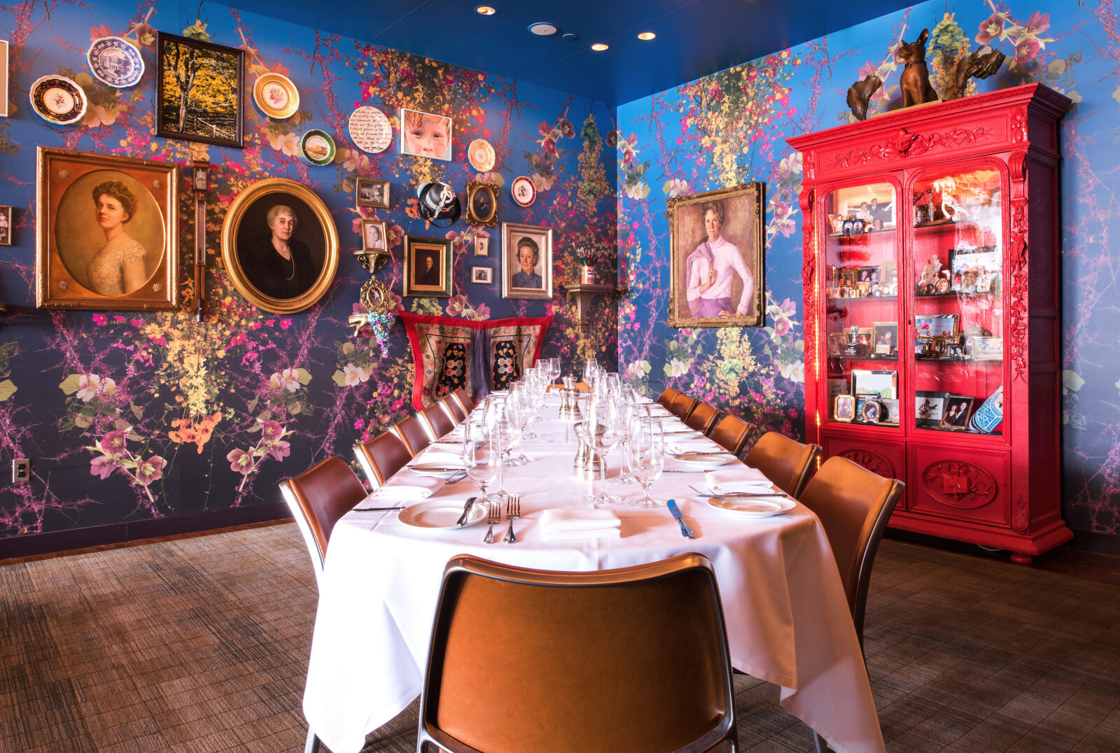 Inside a colorful dining room with floral wallpaper and eclectic artwork on the wall. A set table sits in the middle