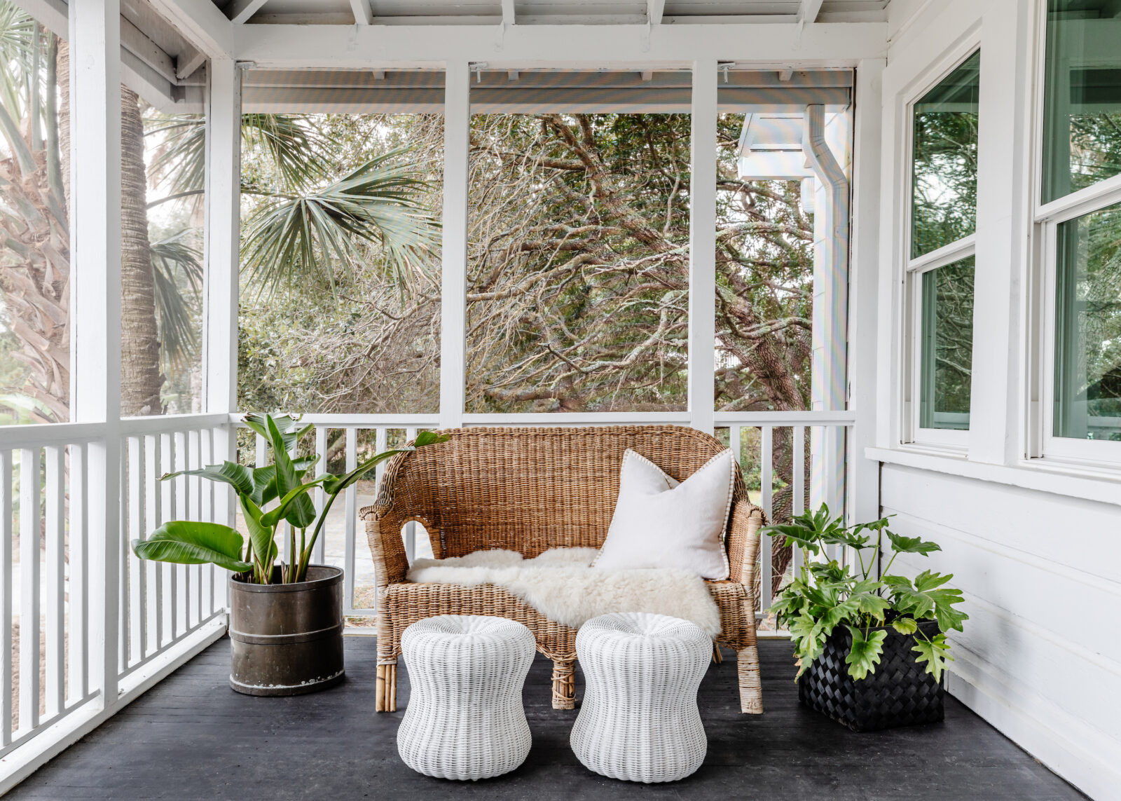A wicker sofa outside on a porch framed by plants