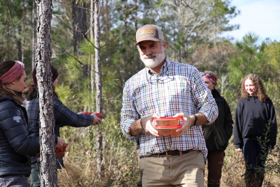A man walks through the woods with two plastic containers