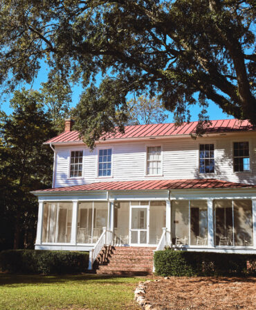 A white farmhouse with a red roof under some trees