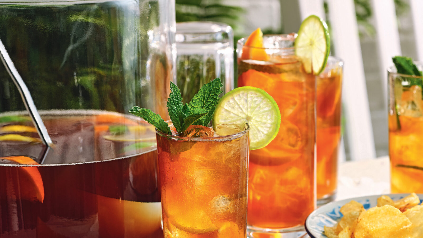Sweet tea punch in a glass with a larger pitcher and sliced oranges