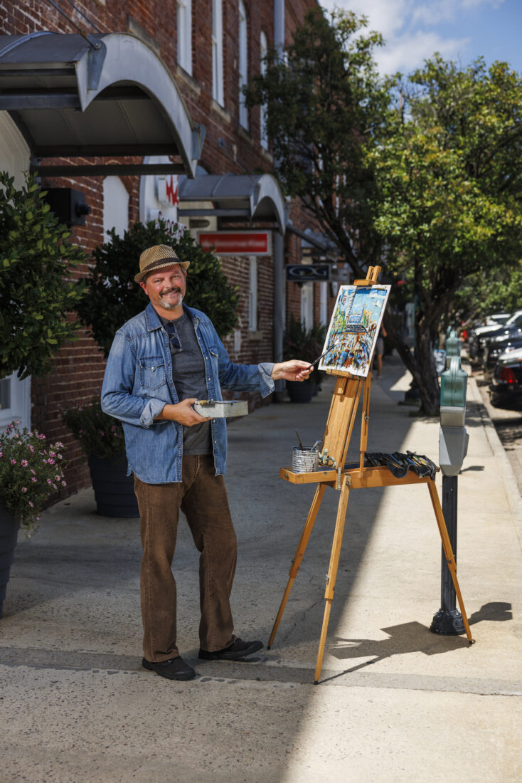 An artist standing at an easel on a sidewalk outside