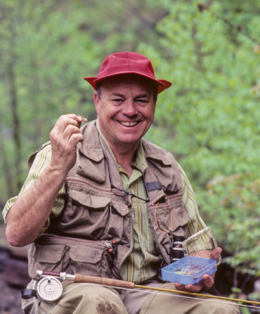 A man sitting in the woods with fly fishing supplies