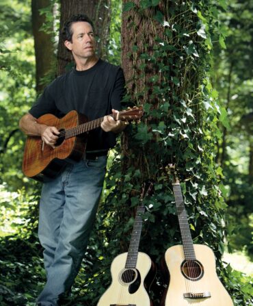 A man holding a guitar beside a tree