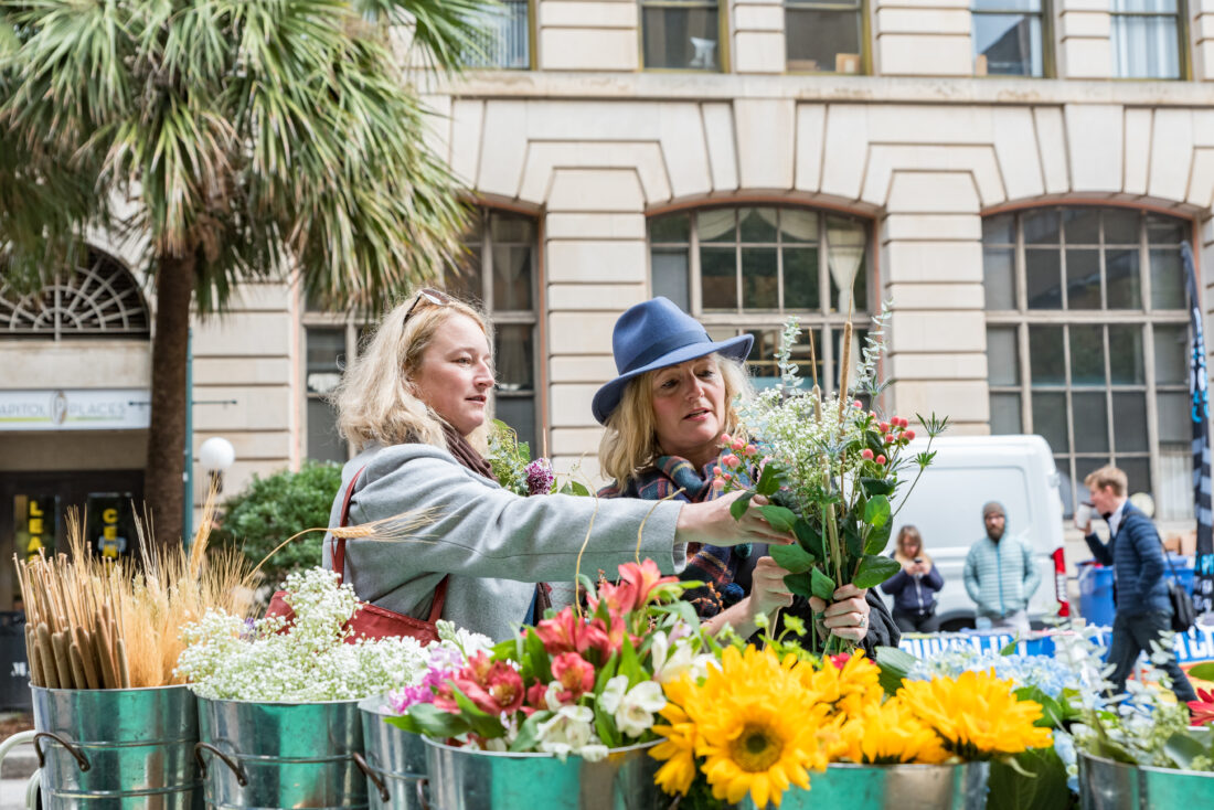 Two women selecting flowers from a stand at an outdoor market