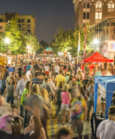 a crowd of people in the street near tents at a festival