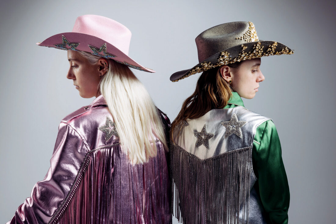 Two musicians in Western wear look over their shoulders