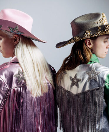 Two musicians in Western wear look over their shoulders