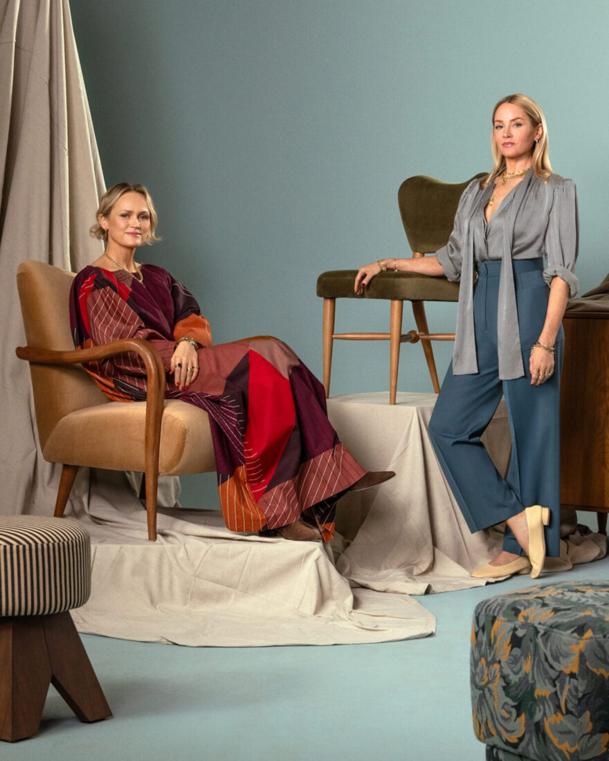 A portrait of two women posed against a collection of furniture