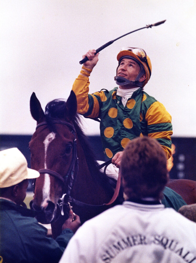 A jockey on a horse raises his crop to the sky