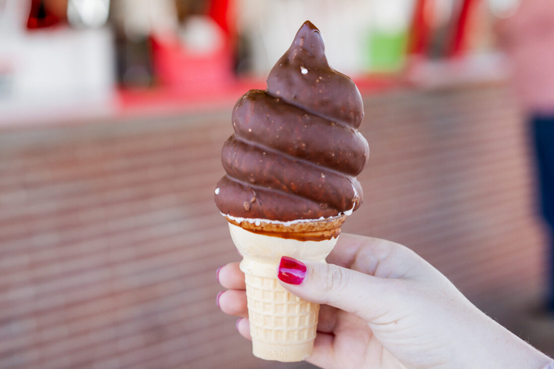 A hand holds a chocolate-dipped ice cream cone