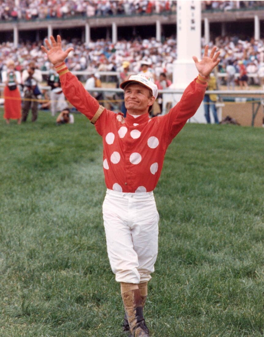 A jockey in a red and white silk raises his arms to the sky