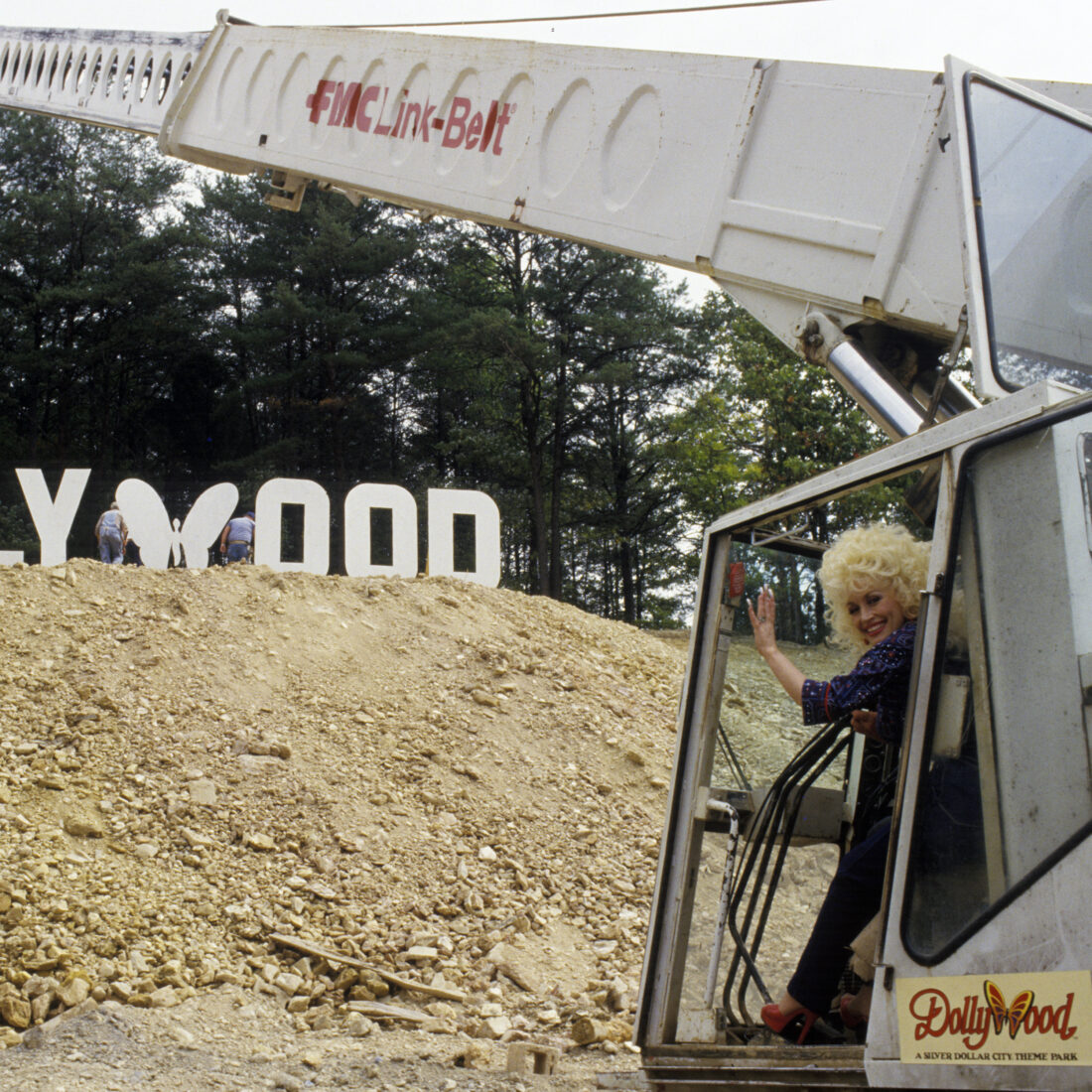 Dolly parton sits in a mechanical machine constructing the dollywood sign