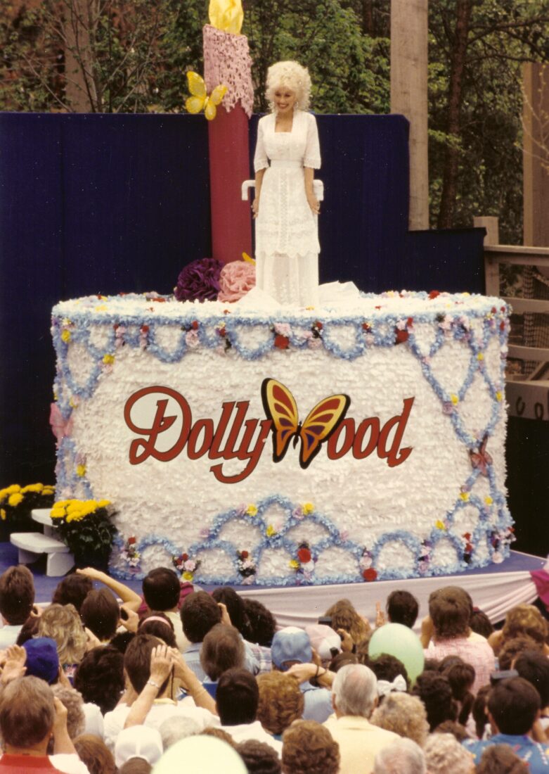 Dolly Parton stands on a Dollywood cake