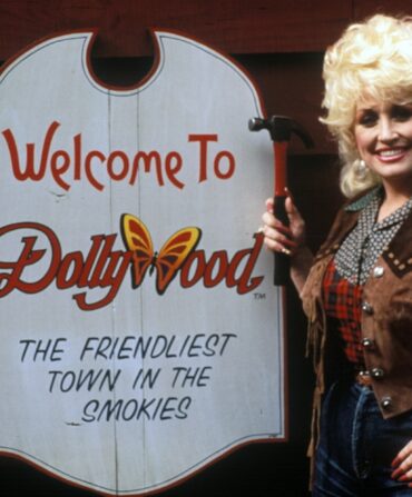 Dolly Parton poses next to a dollywood sign
